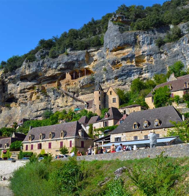 Fransen houden van labels en van afkortingen en met PBVF weten ze beide aardig te combineren. PBVF staat voor Plus Beaux Villages de France, de Mooiste Dorpen van Frankrijk. Nu telt Frankrijk natuurlijk ontzettend veel gemeenten. 35.416 om precies te zijn. Ze zijn vaak niet groot en tellen gemiddeld slechts weinig inwoners. Veel van die dorpjes zijn best mooi, maar 164 ervan zijn bestempeld als wondermooi en kregen het label. En niet minder dan 13 daarvan staan op het programma van onze gasten. Dat wordt keuzes maken! Welke dorpen kunnen PBVF worden? Om Plus Beaux Village de France te worden dien je als dorp een aanvraag in. Let wel, de criteria zijn bijzonder streng: slechts 20% van de aanvragers ontvangt na doorgedreven evaluatie het begeerde label. Er zijn dan ook niet minder dan 30 criteria. Om te weten of het überhaupt de moeite loont om een aanvraag in te dienen kijk je best zorgvuldig naar de eerste drie criteria: je dorp telt niet meer dan 2000 inwoners, je botst er op ten minste twee beschermde sites, zoals een historisch monument of een opmerkelijke erfgoedlocatie én de aanvraag wordt gedragen door de gemeenteraad. Check? Ga dan door naar de volgende ronde. Welke selectiecriteria hanteert de commissie van de PBVF? Vooreerst wordt er gekeken naar de beschermde sites en monumenten in de dorpskern. Dat moeten er dus minstens twee zijn, maar meer mag altijd. Dan worden de architectonische kwaliteiten van het dorp als geheel onder de loep genomen. Harmonie en homogeniteit, daar draait het om. Passen de gebouwde volumes mooi bij elkaar? Is er uniformiteit in de dakbedekkingsmaterialen, de kleuren van de daken, de gevelmaterialen en de gevelkleuren? Mooi. Dan kijken we verder naar de stedenbouwkundige kwaliteiten. Hoe omvangrijk dan wel compact is het bebouwde weefsel? Is ook de omgeving en de toegang tot het dorp de moeite waard? En hoe zit het met de dimensie van het wegennet? Tot slot gaat de commissie na of je als dorp ook actief de nodige inspanningen levert om het geheel nog bijkomend te verfraaien. Wat is het gevoerde beleid aangaande renovatie van gebouwen, reclamepanelen, inrichting van de openbare ruimte, inbreng en beheer van groenelementen? Hoe organiseer je het parkeren in en om het dorp, wat met elektriciteits- en telefoondraden, hoe esthetisch verantwoord is de openbare verlichting?... Verwacht je dus maar aan een lijvig dossier. Liggen er Plus Beaux Villages in de omgeving van Le Manoir? Jazeker, dertien dus… al dient het gezegd dat we, zoals we het hier op het Franse platteland gewoon zijn, ‘omgeving’ best wel ruim interpreteren. Zo ligt ‘onze’ hoofdstad Cahors, de hoofdstad van het departement Lot, op zo’n 70 km. Dat is nu niet meer meteen een dingetje - onze administratie staat tegenwoordig helemaal op punt - maar de eerste jaren zijn we geregeld heen en weer gereden met formulier x en aanvraagblad y (en of we bewijsstuk z misschien ook nog even kunnen binnenbrengen?). Ook voor andere dan onze dagelijkse boodschappen rijden we al snel de ruim 30 km tot Brive-la-Gaillarde. Een concertje in Gramat? 35 km. Een lezing in Milandes? 41 km. Mét bochten. Maar stuk voor stuk schitterende wegen door een wondermooi landschap. We blijven van elke tocht genieten en onze gasten hebben we ook nog niet horen klagen. Daar gaan we dus, richting PBVF… Een overzicht van wat de commissie ons te vertellen heeft, in alfabetische volgorde: Autoire, in het departement Lot, op 44 km van Le Manoir in Souillac Autoire ligt in de holte van een keteldal: een half cirkelvormige vallei die ooit door een gletsjer zou zijn gevormd. Het keteldal wordt omgeven door de ‘causse’ - het kalkplateau - tussen Figeac en Gramat. Hier veel landhuizen en herenhuizen, met consequent bruine dakpannen en een veelheid aan karakteristieke vierkante duiventillen. Een wandeling richting de wand van het keteldal is een must: tijdens nattere perioden klatert er met veel geweld een waterval naar beneden. Verder wandelen tot in Loubresac (zie verder) kan ook. Beynac-et-Cazenac, in het departement Dordogne, op 35 km van Le Manoir in Souillac Beynac-et-Cazenac bevindt zich op 10 km ten zuidwesten van Sarlat-la-Canéda. Het dorp zelf ligt aan de oevers van de Dordogne, maar het meest in het oog springende is het kasteel dat er 150 m bovenuit torent. Het kasteel werd ooit belegerd door Richard Leeuwenhart, en lag nadien tijdens de honderdjarige oorlog vaak en lang in gevecht met het aan de overzijde van de rivier gelegen kasteel van Castelnaud-La-Chapelle (zie verder). Het dorp, met zijn bleke gevels en lauze (kalkstenen) daken oogt vandaag de dag bijzonder vredevol. Carennac, in het departement Lot, op 34 km van Le Manoir in Souillac Carennac dankt zijn bestaan en glorie aan de machtige abdij van Cluny die er in 1047 een priorij sticht. Vanaf de 13de eeuw ontwikkelt zich rond de kerk en de kloostergebouwen een heus dorp. Nu nog hebben tal van huizen hun gebeeldhouwde ramen van weleer behouden. De Romaanse kerk heeft een indrukwekkend 12de eeuws timpaan, het klooster staat er nog, en ook het in de 15de eeuw opgetrokken chateau des Doyens is geklasseerd als historisch monument. Een wandeling in de buurt voert algauw over de restanten van romeinse wegen. Castelnaud-la-Chapelle, in het departement Dordogne, op 38 km van Le Manoir in Souillac Vanuit het kasteel van Castelnaud-la-Chapelle kijk je uit op het kasteel van Beynac. Tussen beide kastelen ligt de Dordogne. In de honderdjarige oorlog vormde die de grens tussen Frankrijk en Engeland. De nu lieflijke vlakte tussen beide kastelen was dus jarenlang een gevaarlijk oorlogsterrein. Het kasteel van Castelnaud is nu omgebouwd tot een museum voor Middeleeuwse oorlogsvoering. Nog in Castelnaud-la-Chapelle bevindt zich het kasteel van Milandes, voormalig eigendom van Josephine Baker. De huidige eigenaars doen er alles aan om het leven van deze grande dame in de kijker te zetten. Prachtige collectie én een mooi maar triest verhaal. Collonge-la-Rouge, in het departement Corrèze, op 34 km van Le Manoir in Souillac Collonge-la-Rouge, met zijn silhouet van purpere kalksteen, rijst van ver duidelijk zichtbaar op tussen het omgevende groen. In het compact dorp met imposante bouwvolumes, bekroond met leistenen daken en tal van torentjes, getuigt elke steen van een rijke geschiedenis. Ooit was het een stopplaats voor pelgrims op weg naar Santiago de Compostela, en daar heeft het nog zijn 11de eeuwse kerk aan te danken. Op de oude graan- en wijnmarkt uit de 16de eeuw staat nog steeds de gemeenschappelijke oven die herinnert aan de bloeitijd van deze handelsstad. In de 19de eeuw zorgde de druifluisepidemie voor een compleet verval, om pas in de jaren ‘80 van de vorige eeuw een nieuwe adem te vinden. Curemonte, in het departement Corrèze, op 37 km van Le Manoir in Souillac Curemonte strekt zich uit op een lange heuvelrug die uitkijkt over de valleien van de Soudroire en de Maumont. Curemonte heeft als bijnaam ‘Village des Trois’, want hoe schattig klein het dorpje ook is, er staan drie kastelen, drie kerken en drie bronnen. Het zijn vooral de centraal en naast elkaar gelegen kastelen van Saint-Hilaire (14de eeuw) met zijn vierkante torens, en het kasteel van Les Plas (16de eeuw) met zijn ronde torens, die in het oog springen. Ze zijn dan ook van dezelfde eigenaar en liggen binnen dezelfde ommuurde tuin. Het derde kasteel, La Johannie, bevindt zich net naast de dorpshal. Breng zeker ook een bezoek aan de oriëntatietafel net buiten en boven het dorp, met zicht over de daken van Curemonte en het weidse landschap eromheen. Domme, in het departement Dordogne, op 34 km van Le Manoir in Souillac Domme werd rond 1280 uitgebouwd als ‘bastide’, een vestingstadje van strategisch belang in de oorlog tussen Fransen en Engelsen. Domme's bijzondere kenmerk en onmiskenbare charme is zijn ligging op de klif, met uitzicht op de Dordogne. In het verlengde van de Place de la Halle ligt de esplanade de la Barre, die 150 meter boven de mythische rivier uitsteekt en een panoramisch uitzicht biedt op de landschappen van de vallei, gekenmerkt door gecultiveerde vlaktes en de zeer donkergroene eikenbossen waaraan dit deel van de Périgord zijn label 